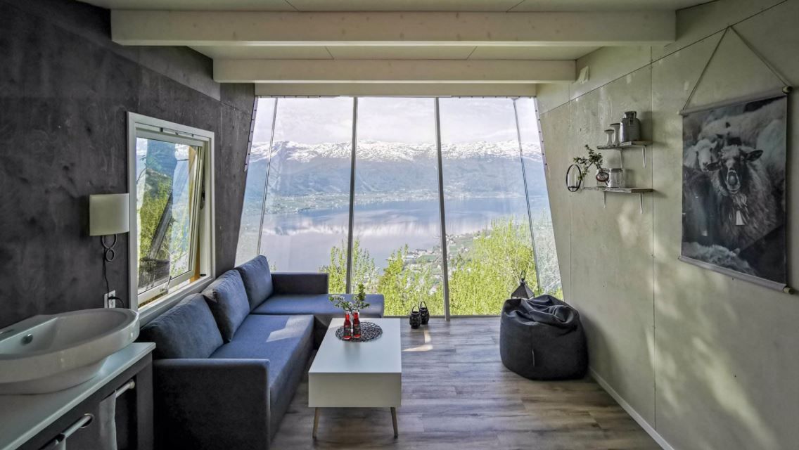 Cozy modern room with sofa, coffee table, beanbag, and large windows overlooking a lake and snowy mountains..