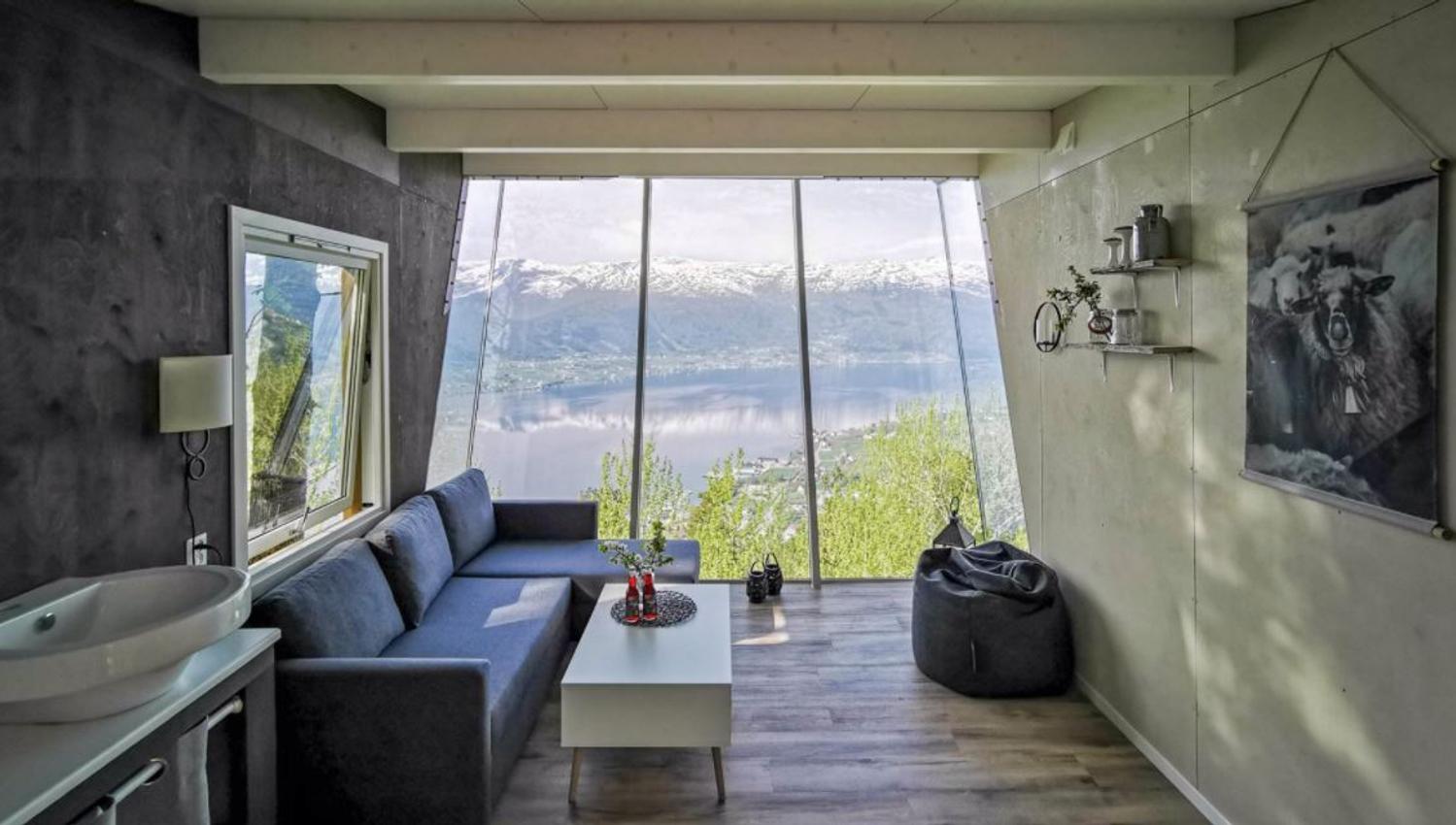 Cozy modern room with sofa, coffee table, beanbag, and large windows overlooking a lake and snowy mountains..