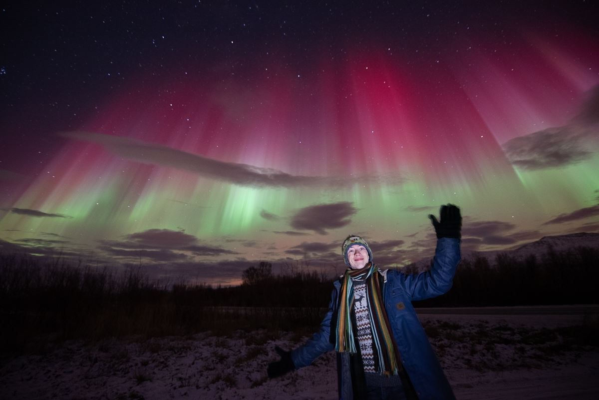 A guest gives a friendly gesture to the Northern Lights, showing in red, green and white colours