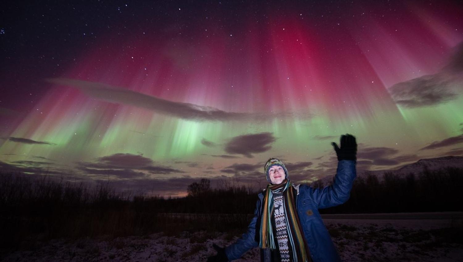 A guest gives a friendly gesture to the Northern Lights, showing in red, green and white colours
