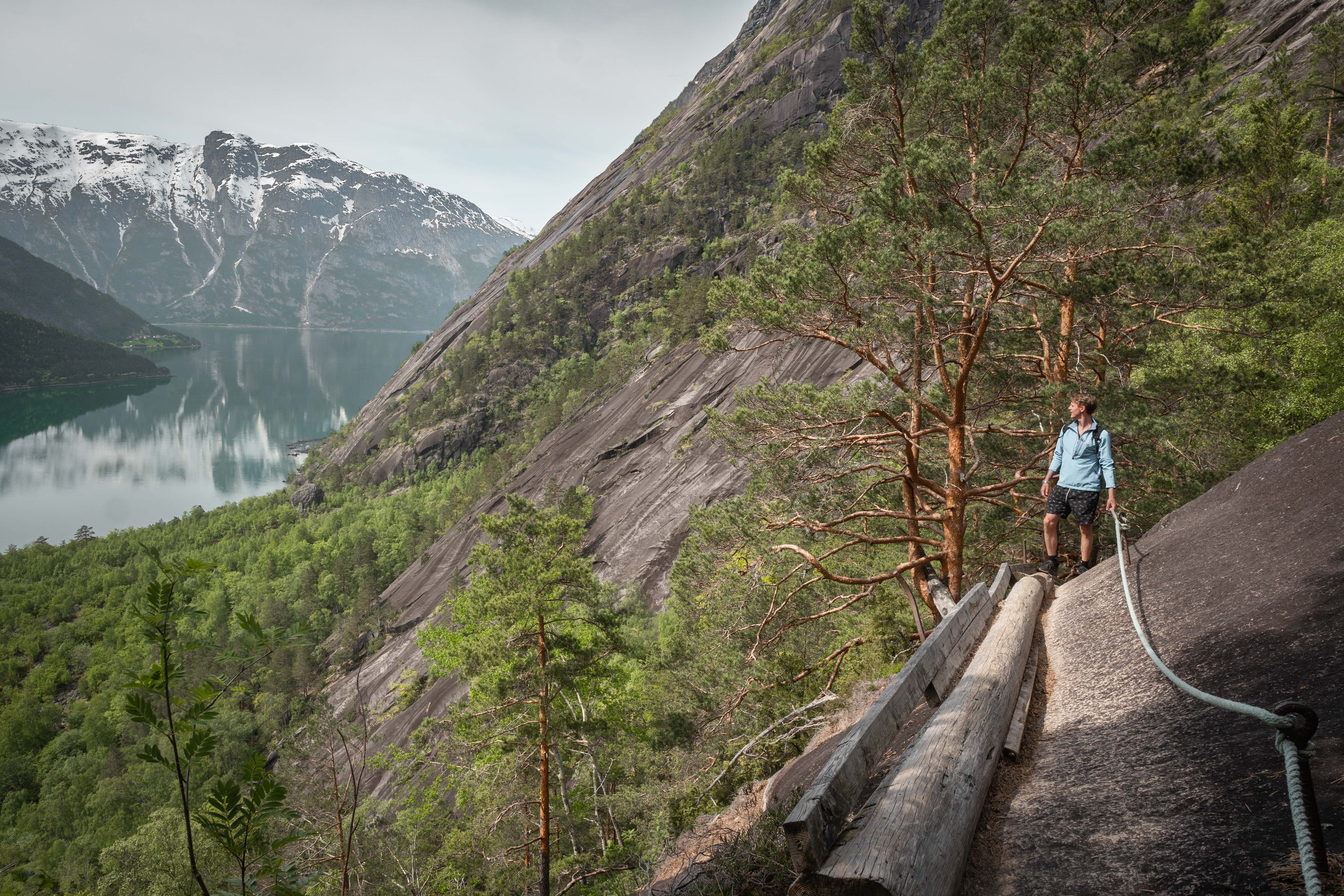 A hiker crossing the mountain side on a wooden timber log boltet in to the mountain wall.