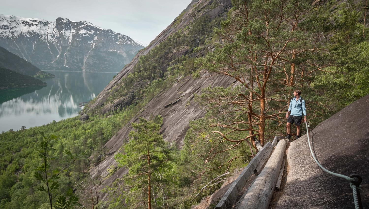 A hiker crossing the mountain side on a wooden timber log boltet in to the mountain wall.
