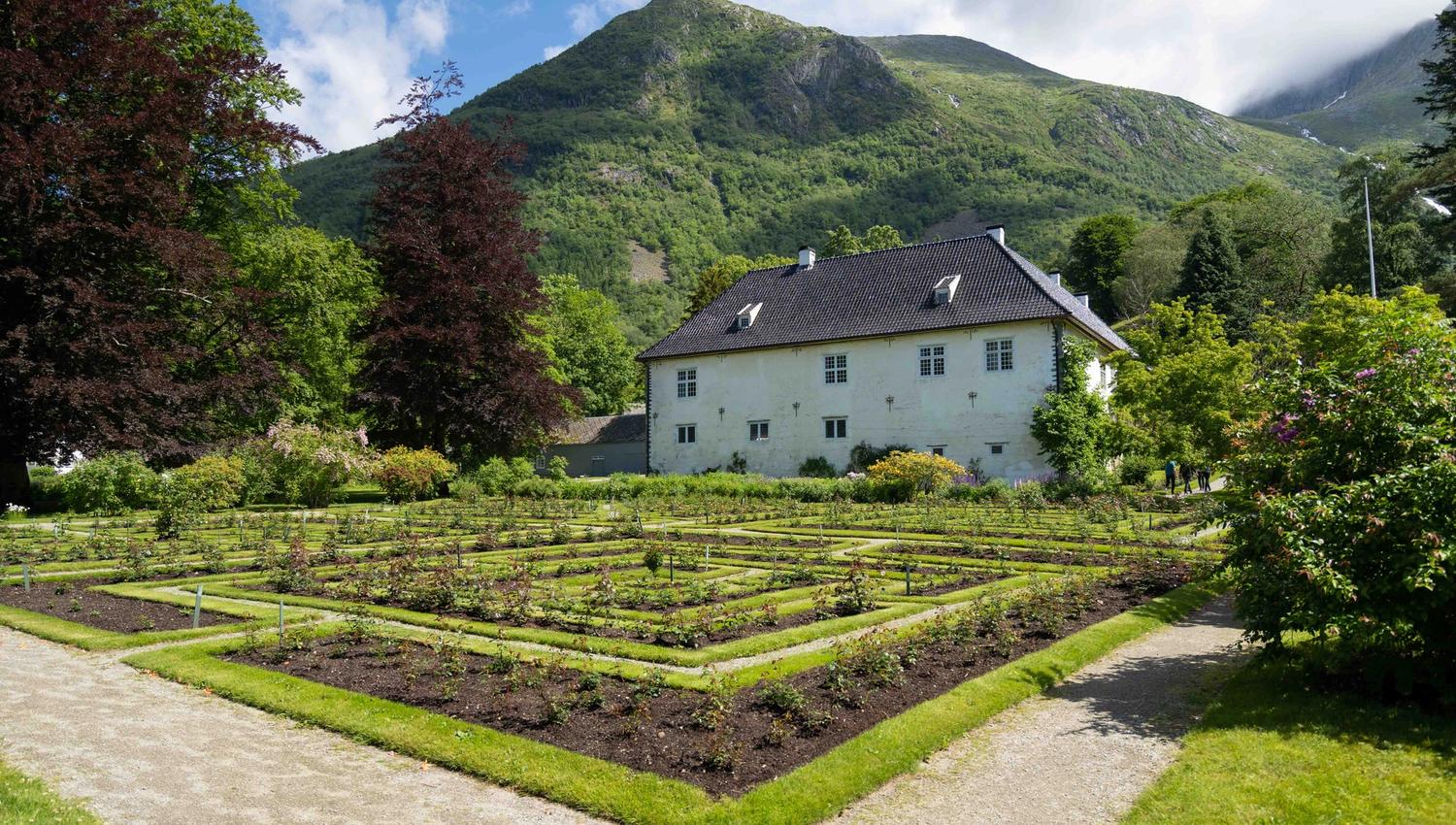 Beautiful garden and historic building at Baroniet in Rosendal, surrounded by green landscape and mountains.