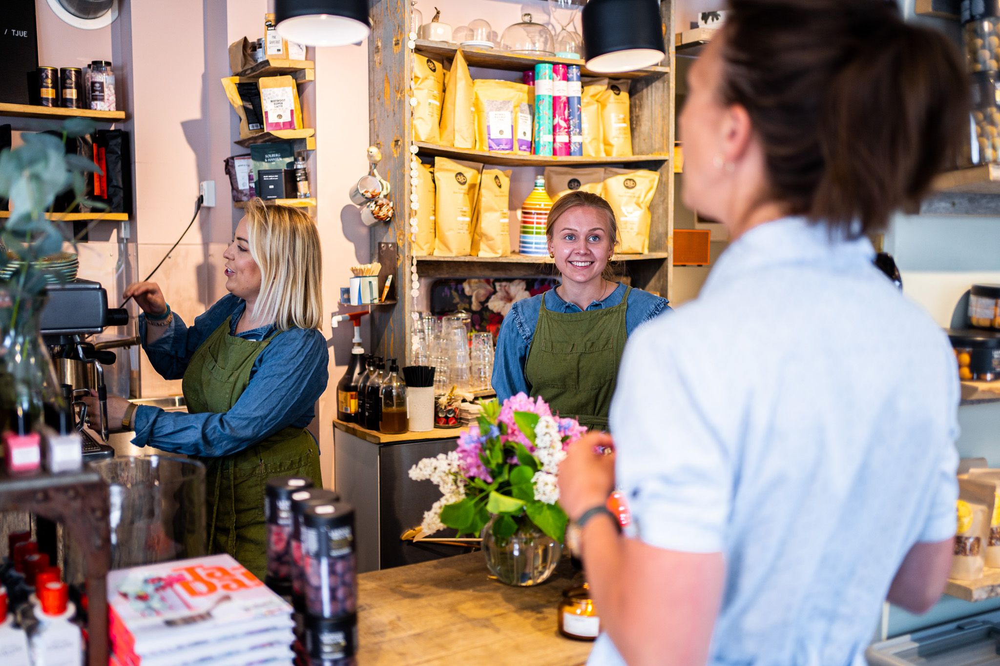 two women working at a store while talking with a customer