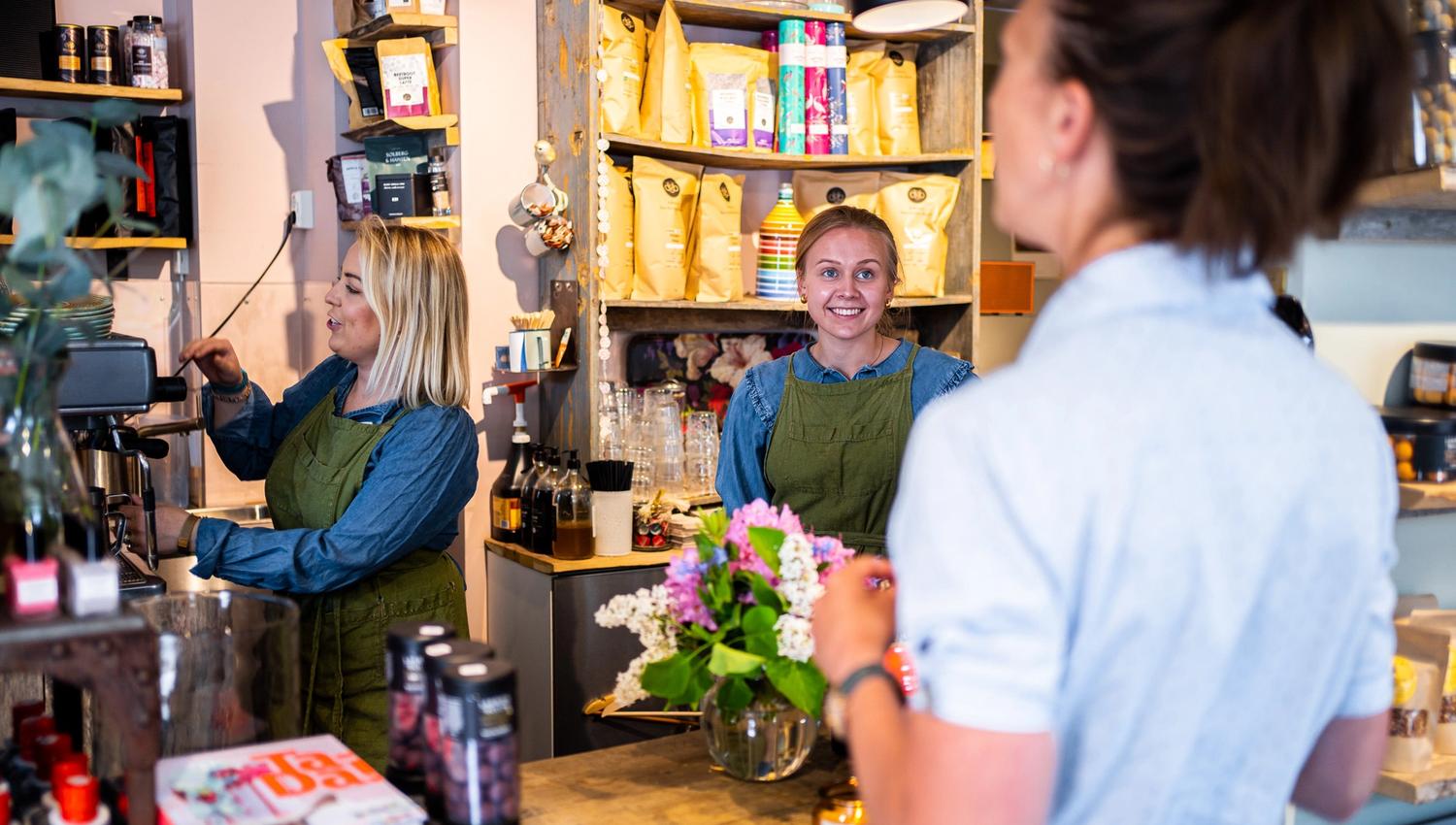 two women working at a store while talking with a customer