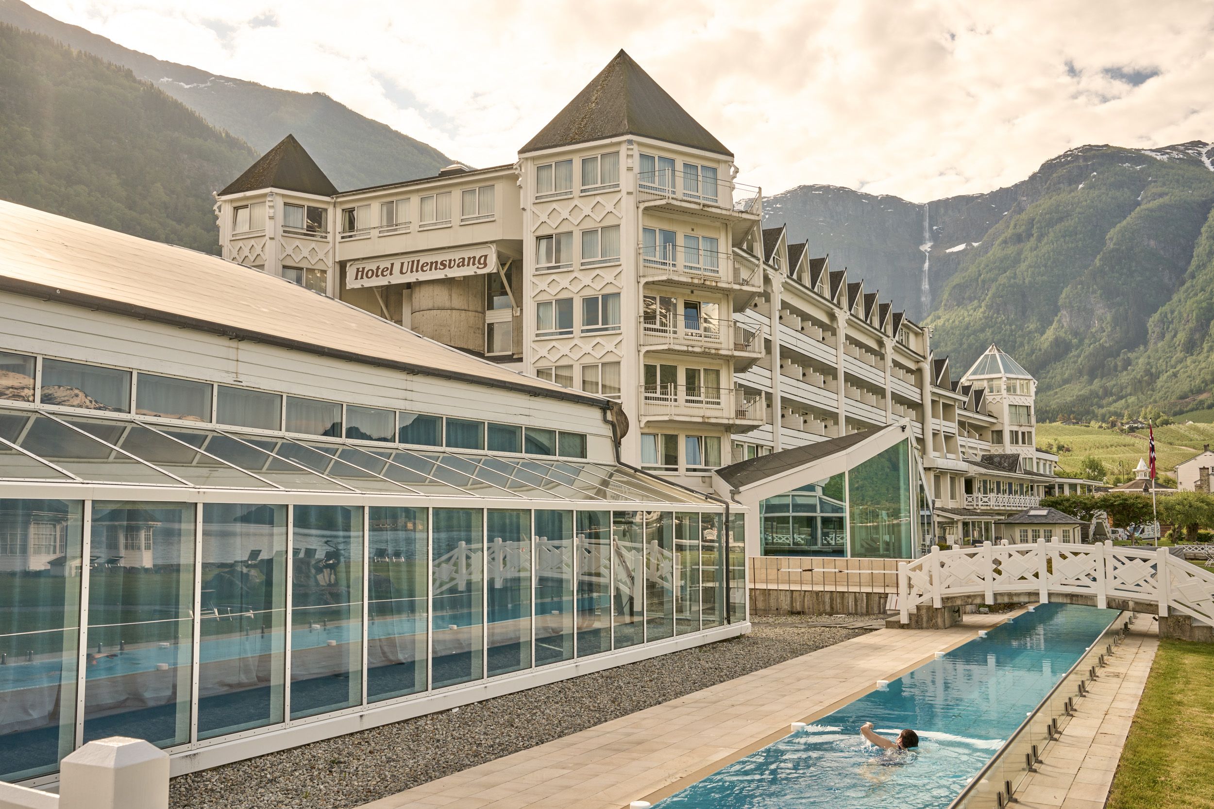 Guest enjoying the long outdoor pool with stunning views of the Hardangervidda mountains behind Hotel Ullensvang.
