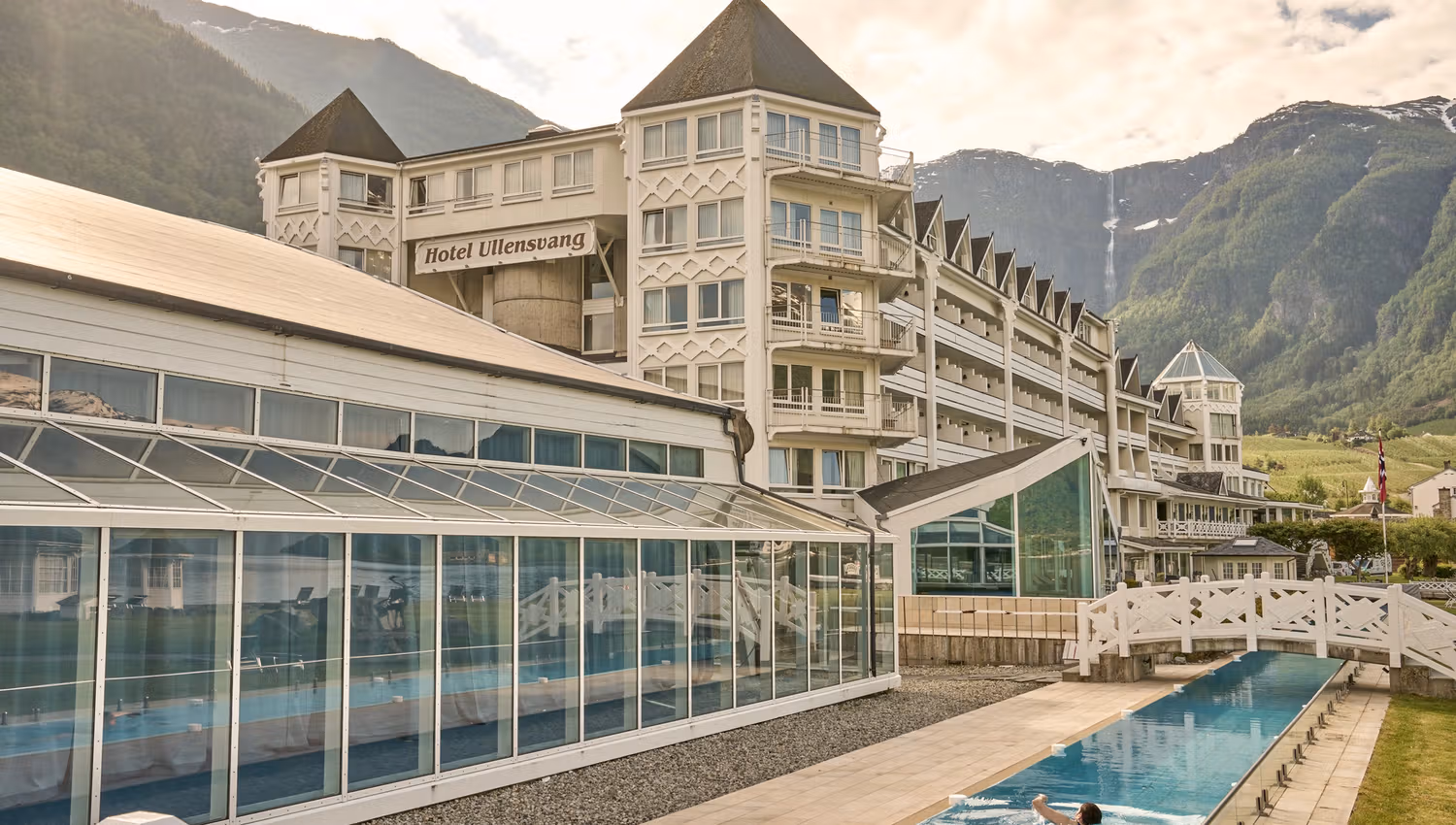 Guest enjoying the long outdoor pool with stunning views of the Hardangervidda mountains behind Hotel Ullensvang.