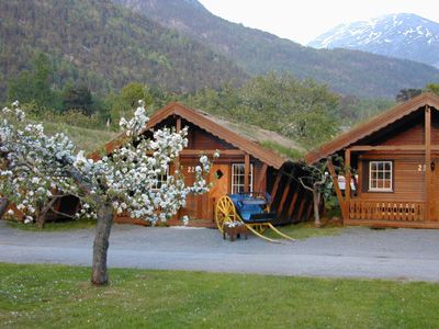 Charmante Blockhütten in wunderschöner Umgebung im Mikkelparken Ferietun, mit blühenden Obstbäumen und Bergen im Hintergrund.