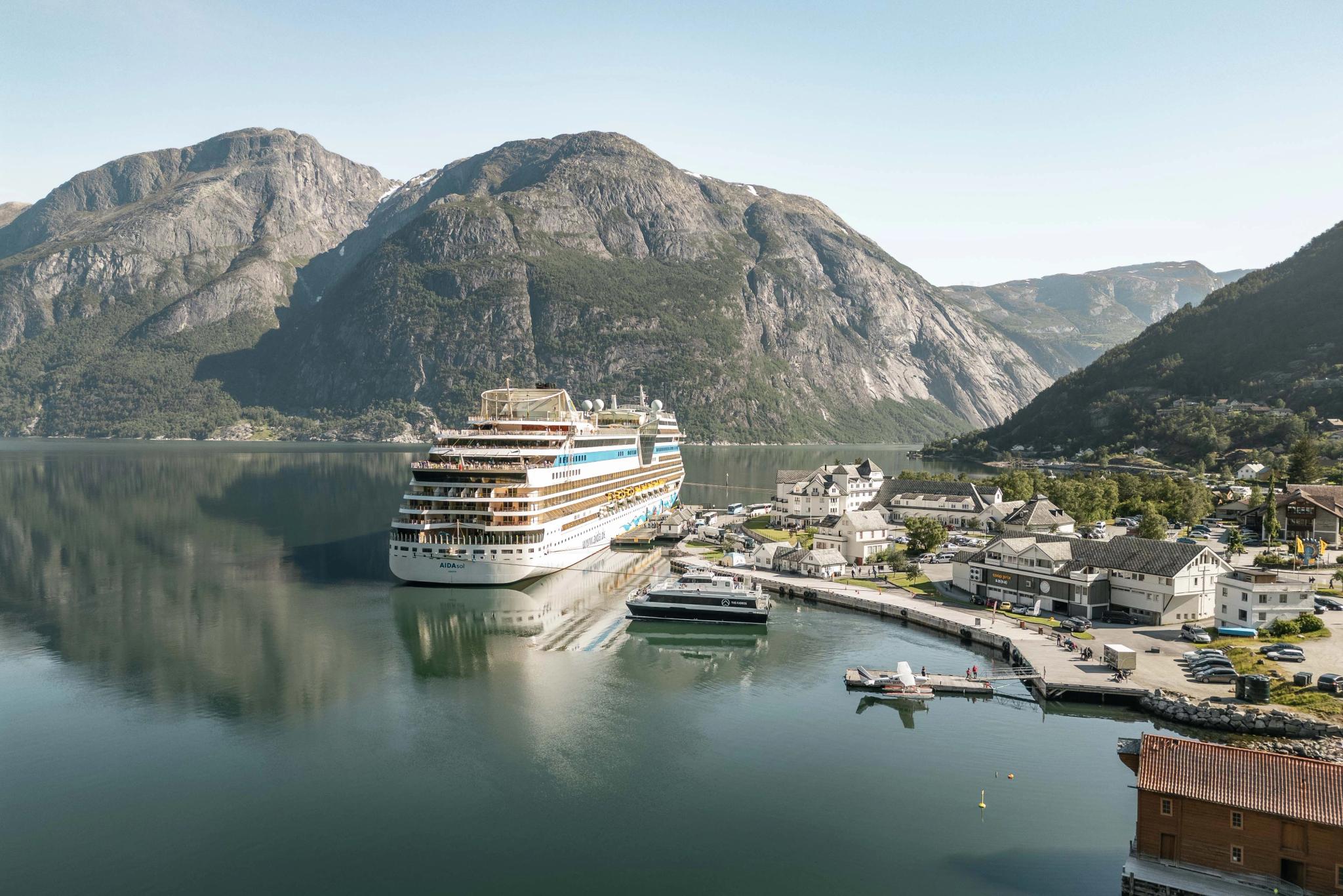 The harbour area with a cruise ship, a smaller vessel, a seaplane and people on the dock.
