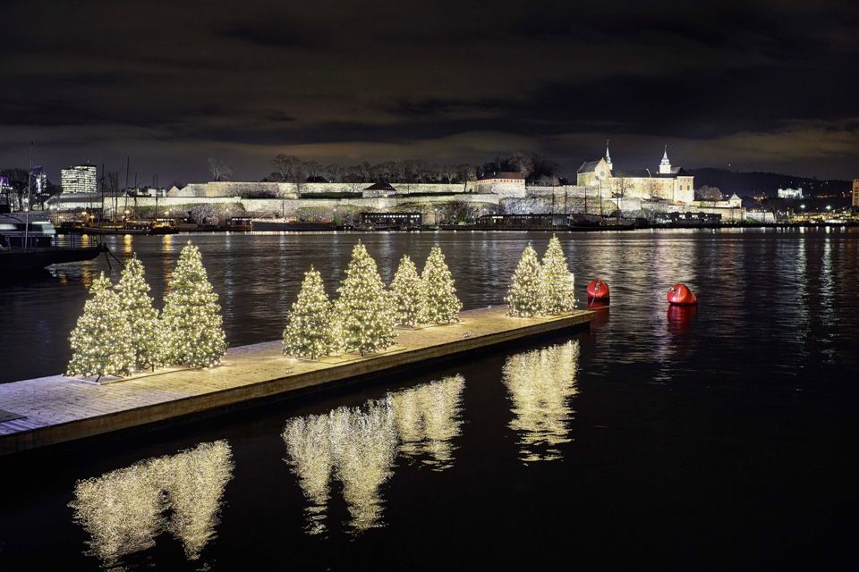 Night photo of a pier with lit Christmas trees. Akershus Fortress in the background.