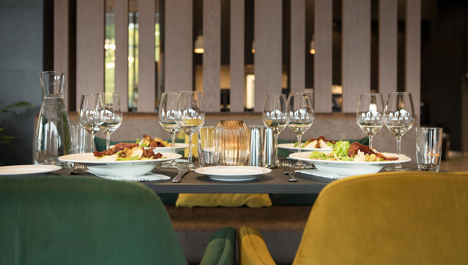 The picture shows a nicely set table in a modern restaurant. There are plates with food, several wine glasses, water glasses, and cutlery on the table