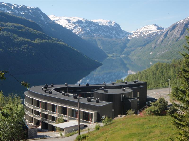 Hordatun Hotel in a summer setting, overlooking Røldalsvatnet with snow-covered peaks in the background.
