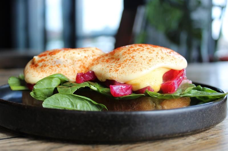 Eggs Benedict served on bread with spinach, pickled vegetables and hollandaise sauce. The dish is part of the breakfast or brunch menu.