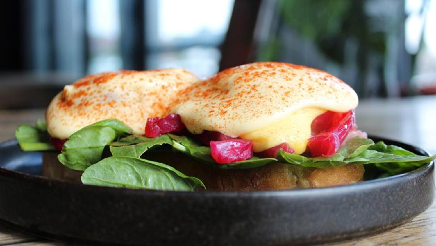 Eggs Benedict served on bread with spinach, pickled vegetables and hollandaise sauce. The dish is part of the breakfast or brunch menu.