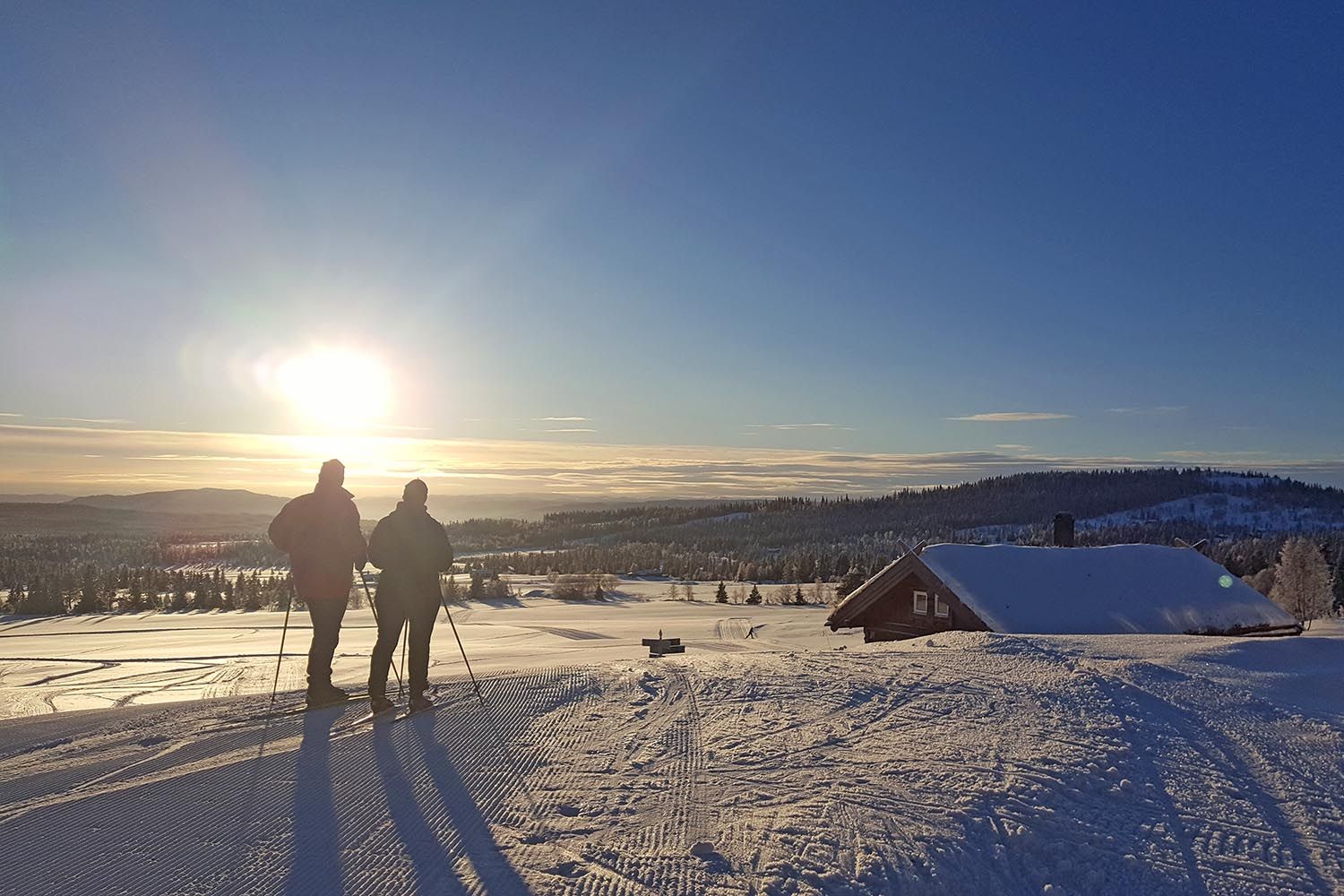 To personer i kveldslys i skiløype ved en hytte