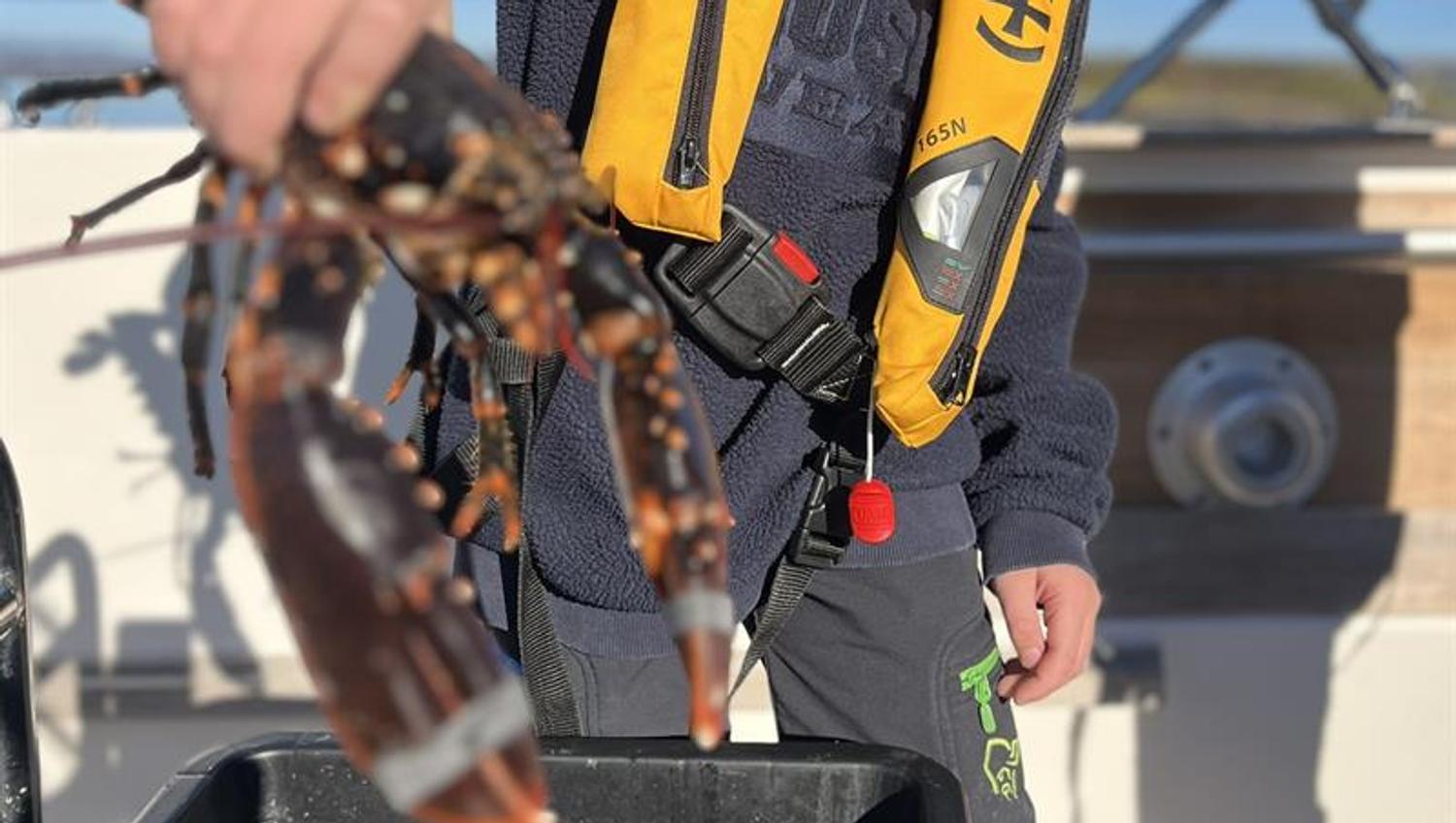 A child holds a lobster over a bucket on the deck of a boat.