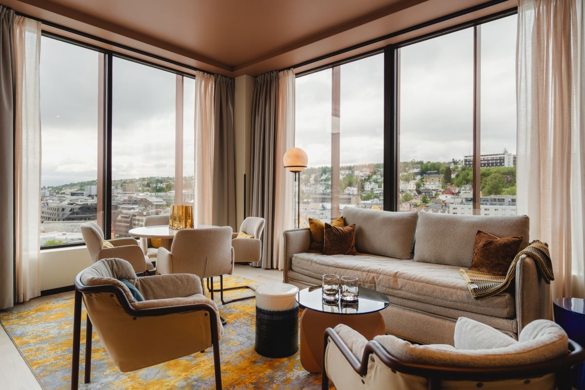 Stue med store vinduer, beige sofa og utsikt mot by og grøntområde