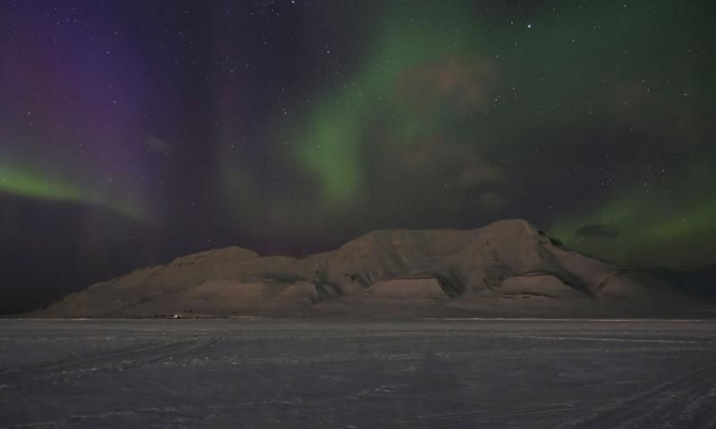 Snow covered mountains with purple and green northern lights in the sky above.