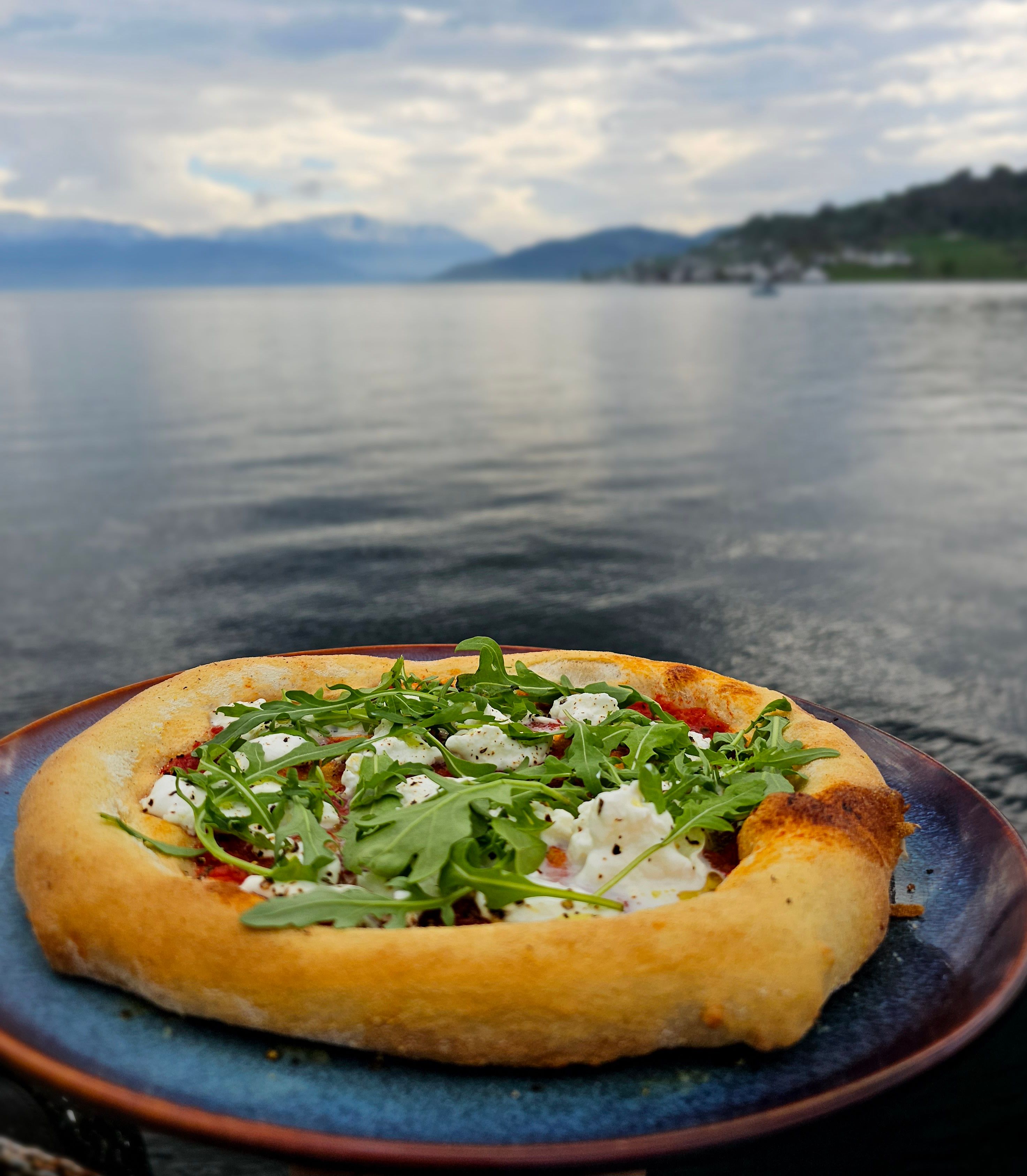 Wood-fired pizza with arugula served with a view of the fjord and mountains.