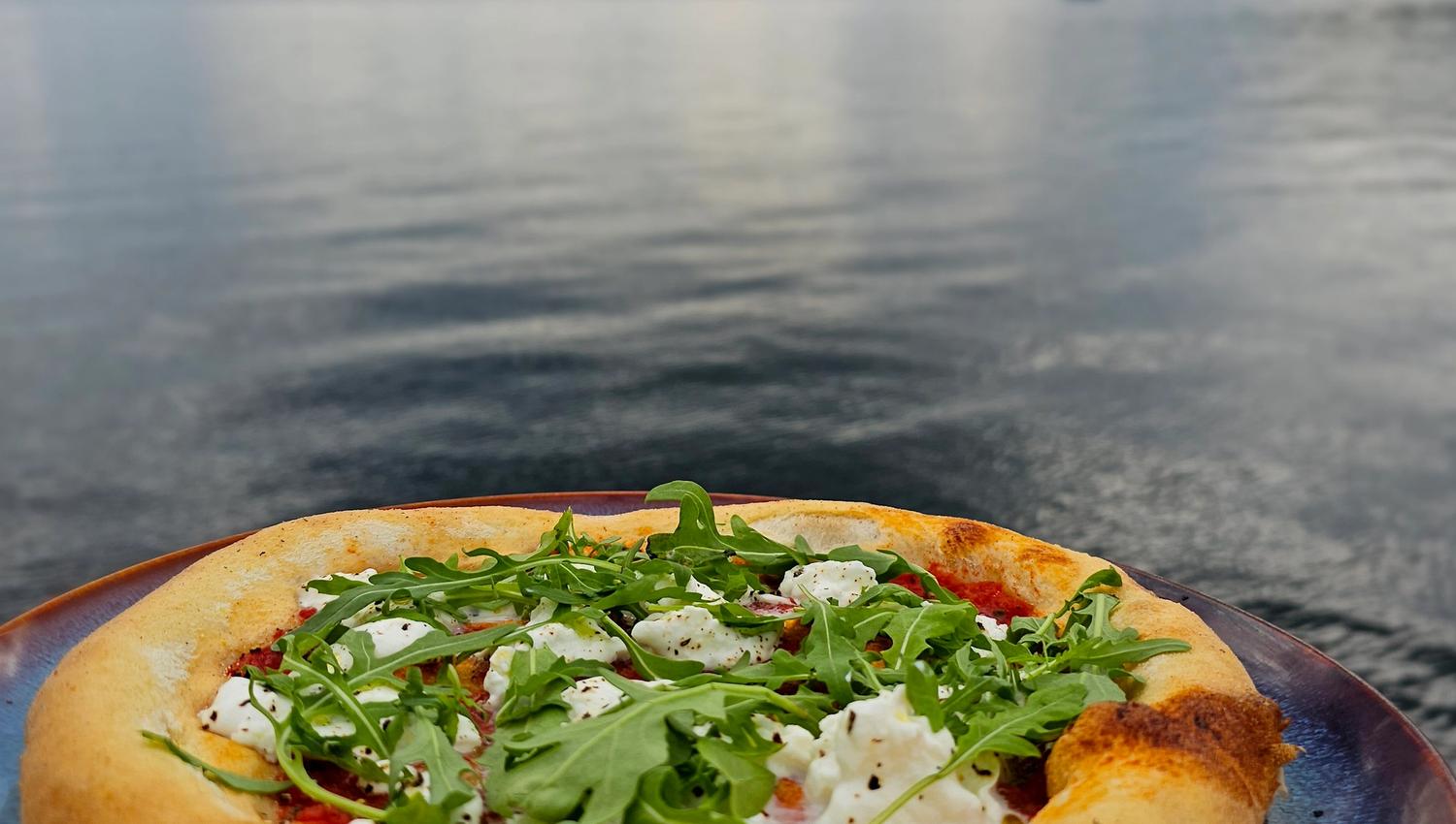 Wood-fired pizza with arugula served with a view of the fjord and mountains.