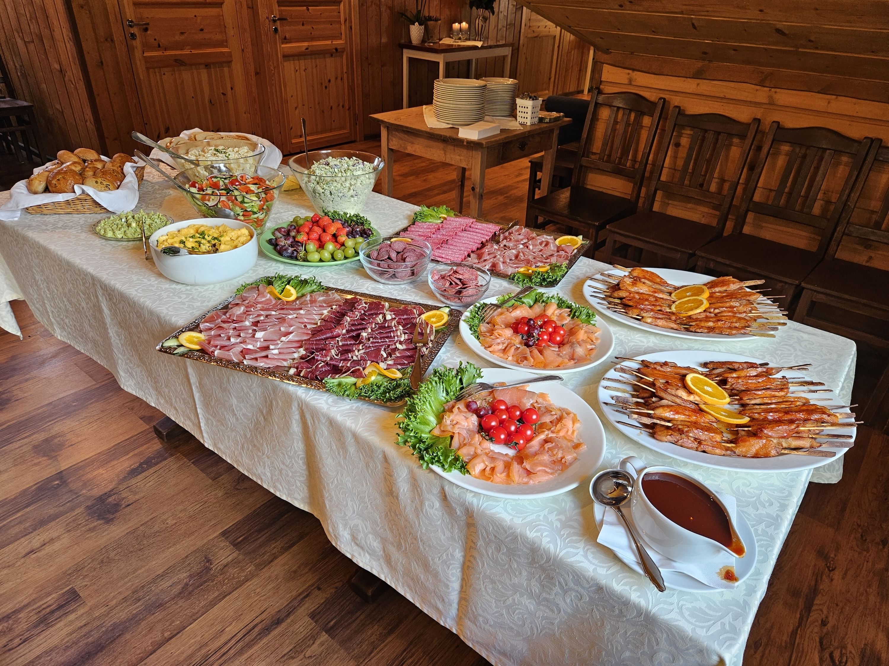 A buffet table set with salads, bread, sliced meats, smoked fish, shrimp skewers, fruit, and sauce in a wooden room at Aabrekk Gard Trollbu in Oldedalen valley.