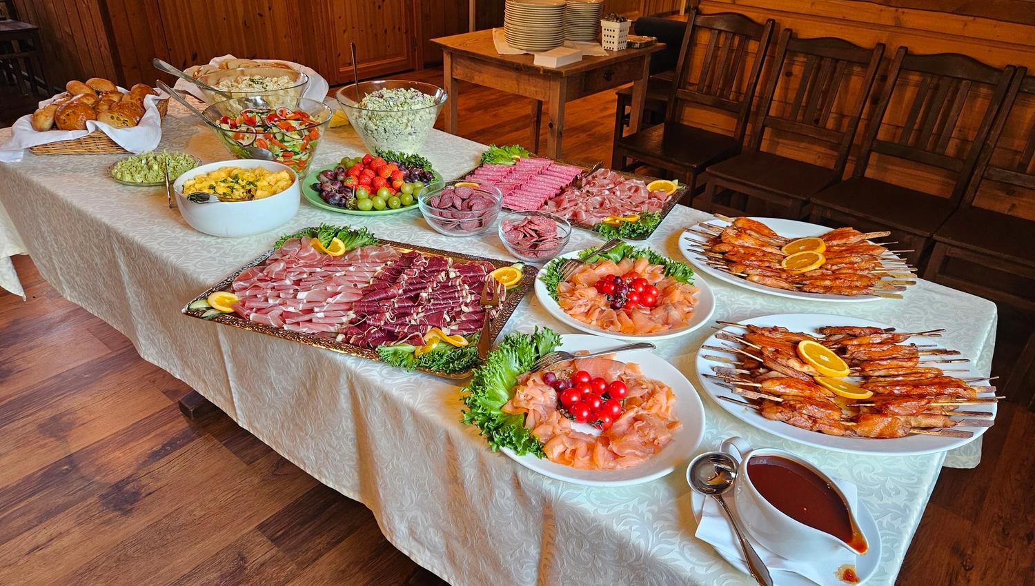 A buffet table set with salads, bread, sliced meats, smoked fish, shrimp skewers, fruit, and sauce in a wooden room at Aabrekk Gard Trollbu in Oldedalen valley.