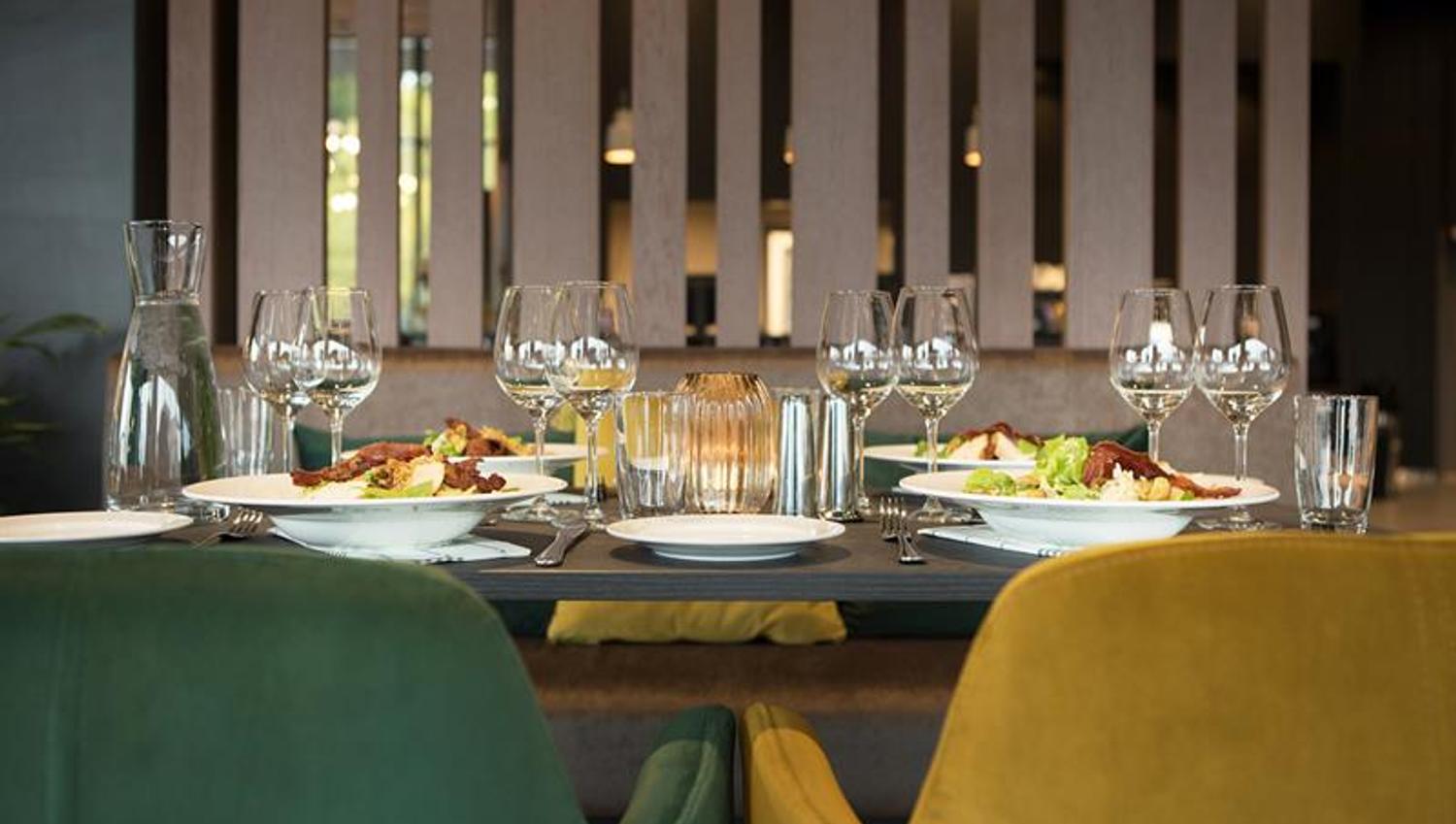 The picture shows a nicely set table in a modern restaurant. There are plates with food, several wine glasses, water glasses, and cutlery on the table