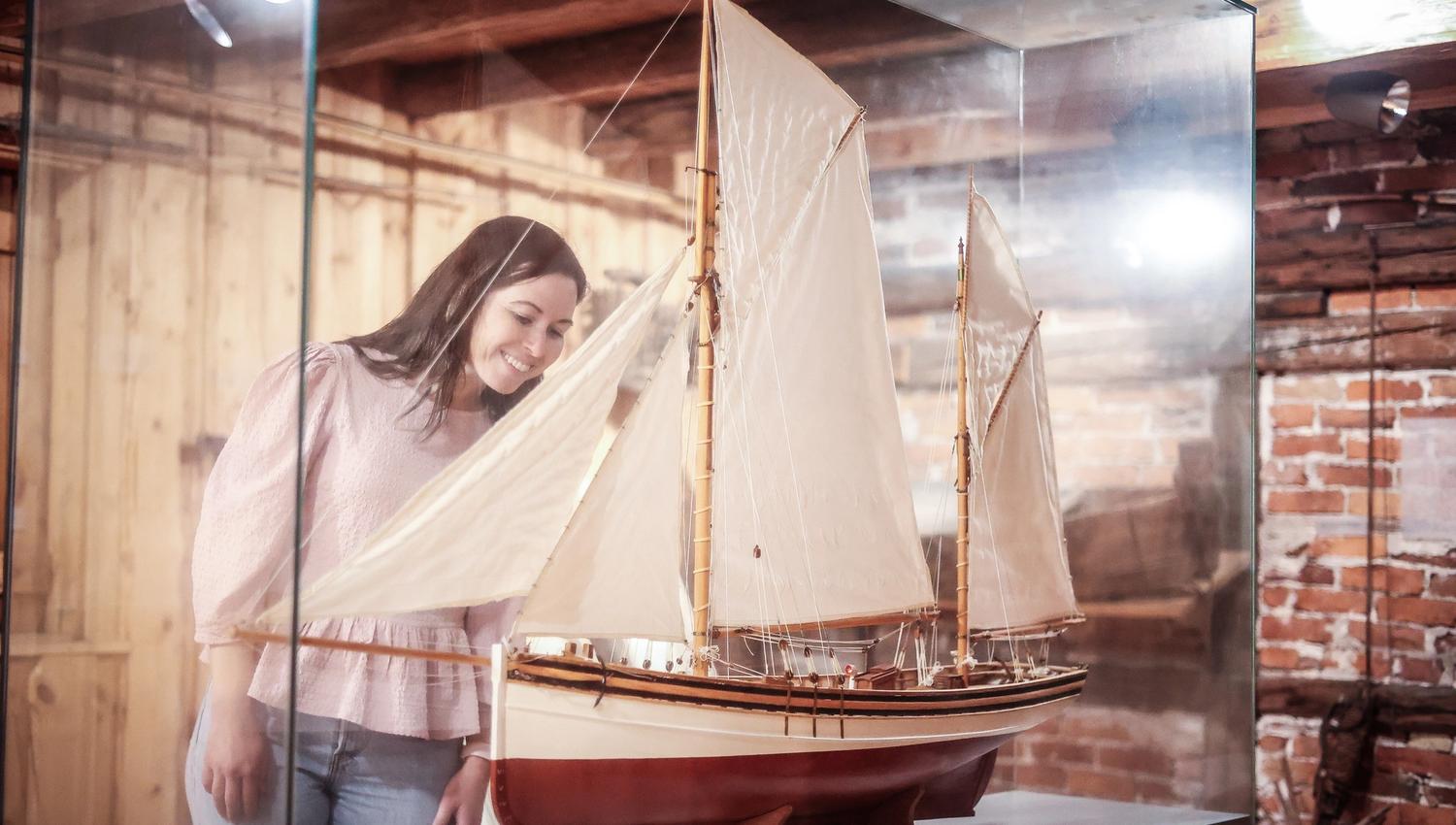 A smiling lady is looking at a miniature ship