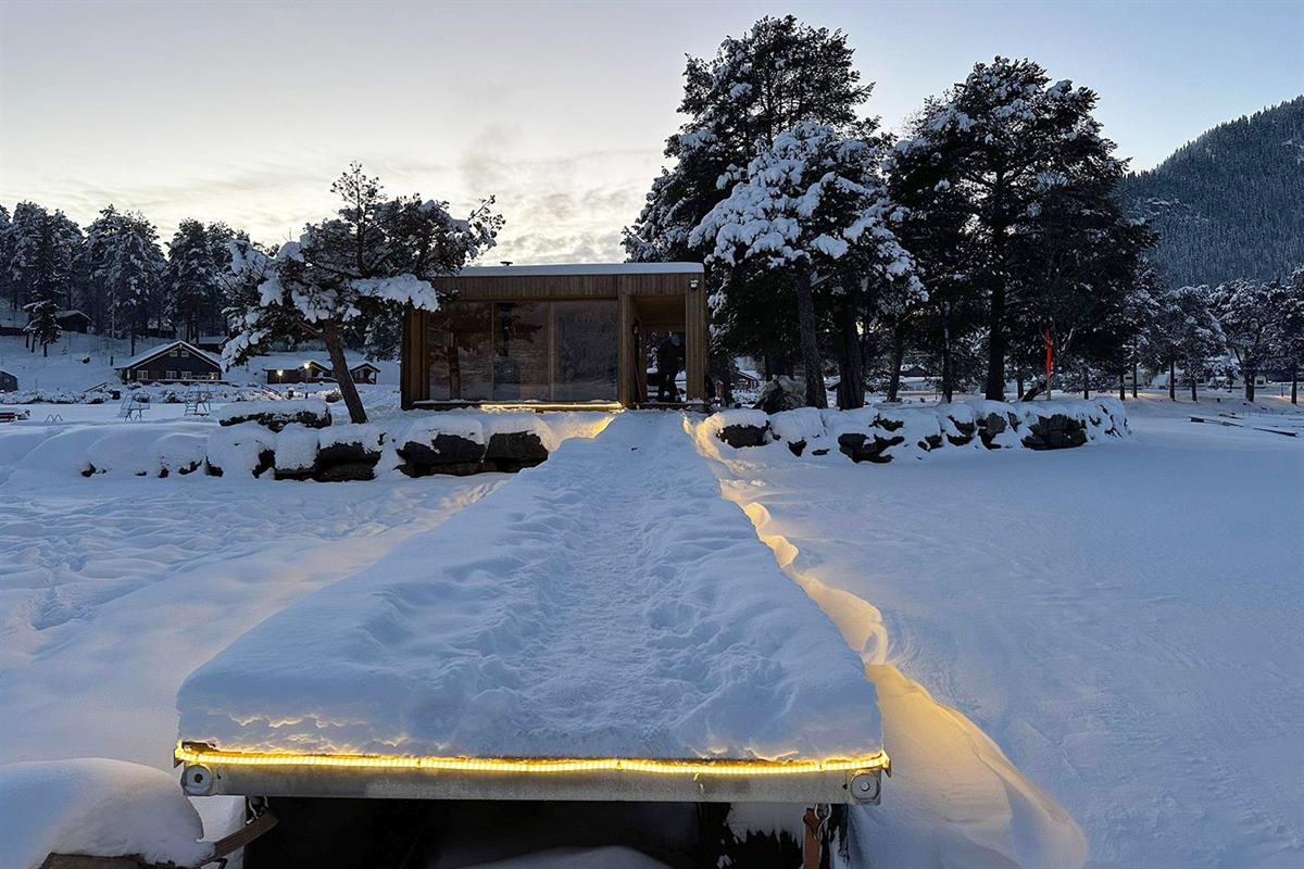Badstu ved innsjø med opplyst badebrygge om vinteren i dyp snø