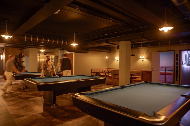 Three pool tables with people playing at one of them.