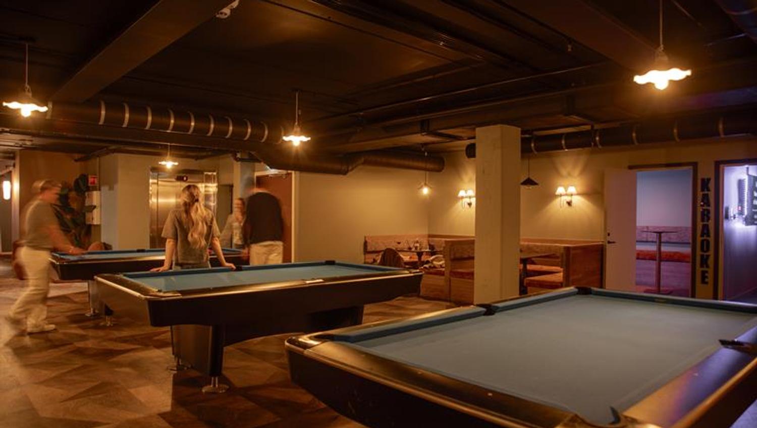 Three pool tables with people playing at one of them.