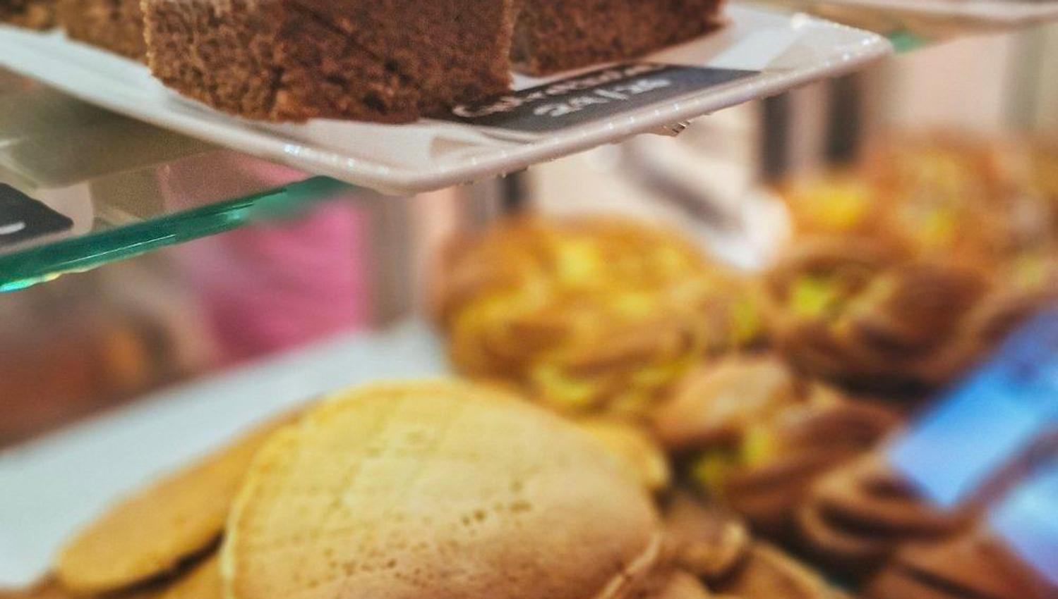 Close-up of pancakes stacked in a bakery display case, with frosted cake slices on a tray above and pastries behind.