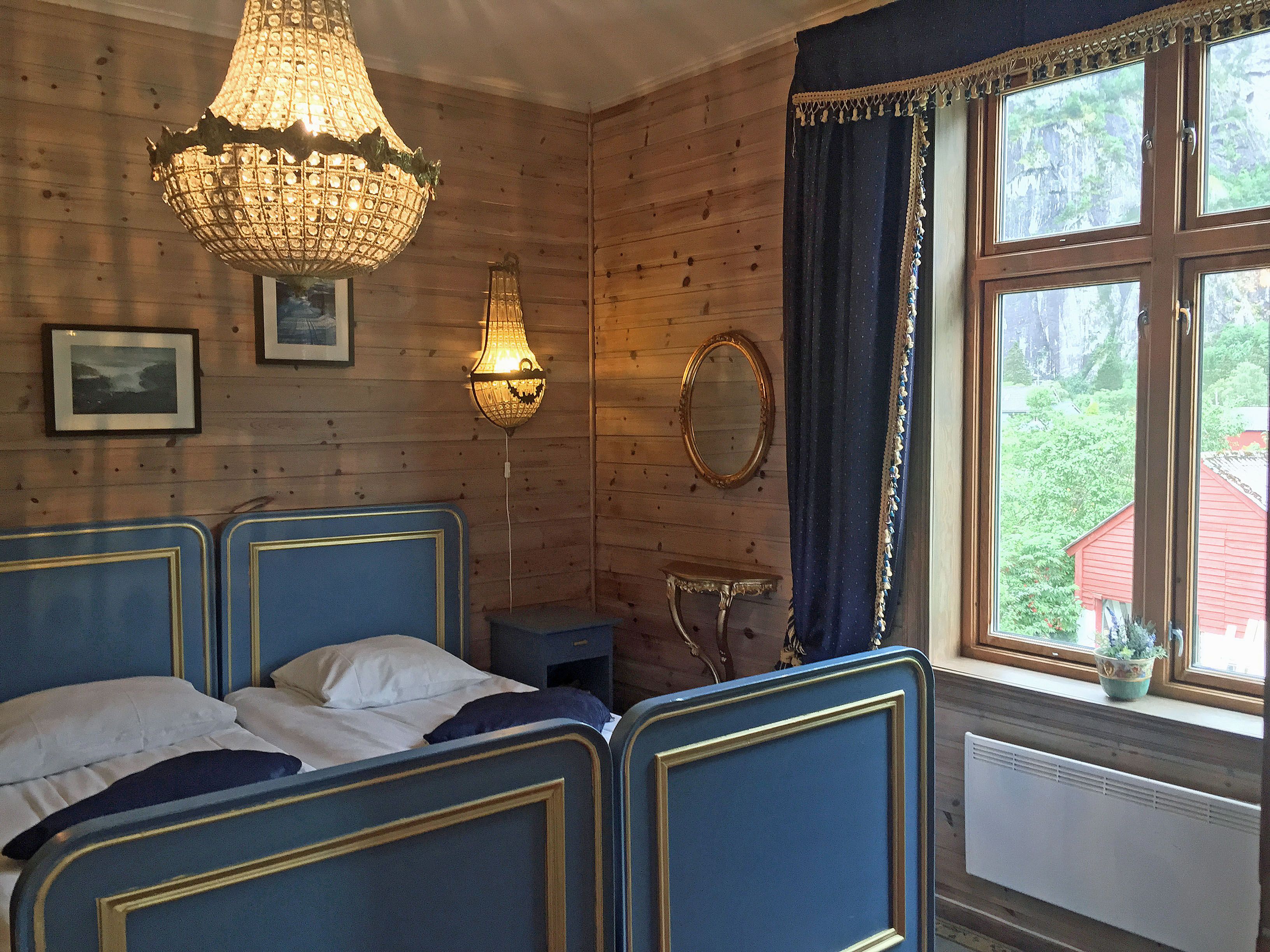 A room with a double bed, blue details and a big chandelair hanging above the bed.