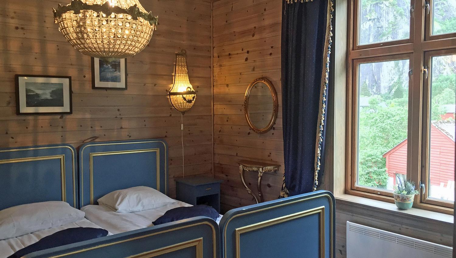 A room with a double bed, blue details and a big chandelair hanging above the bed.