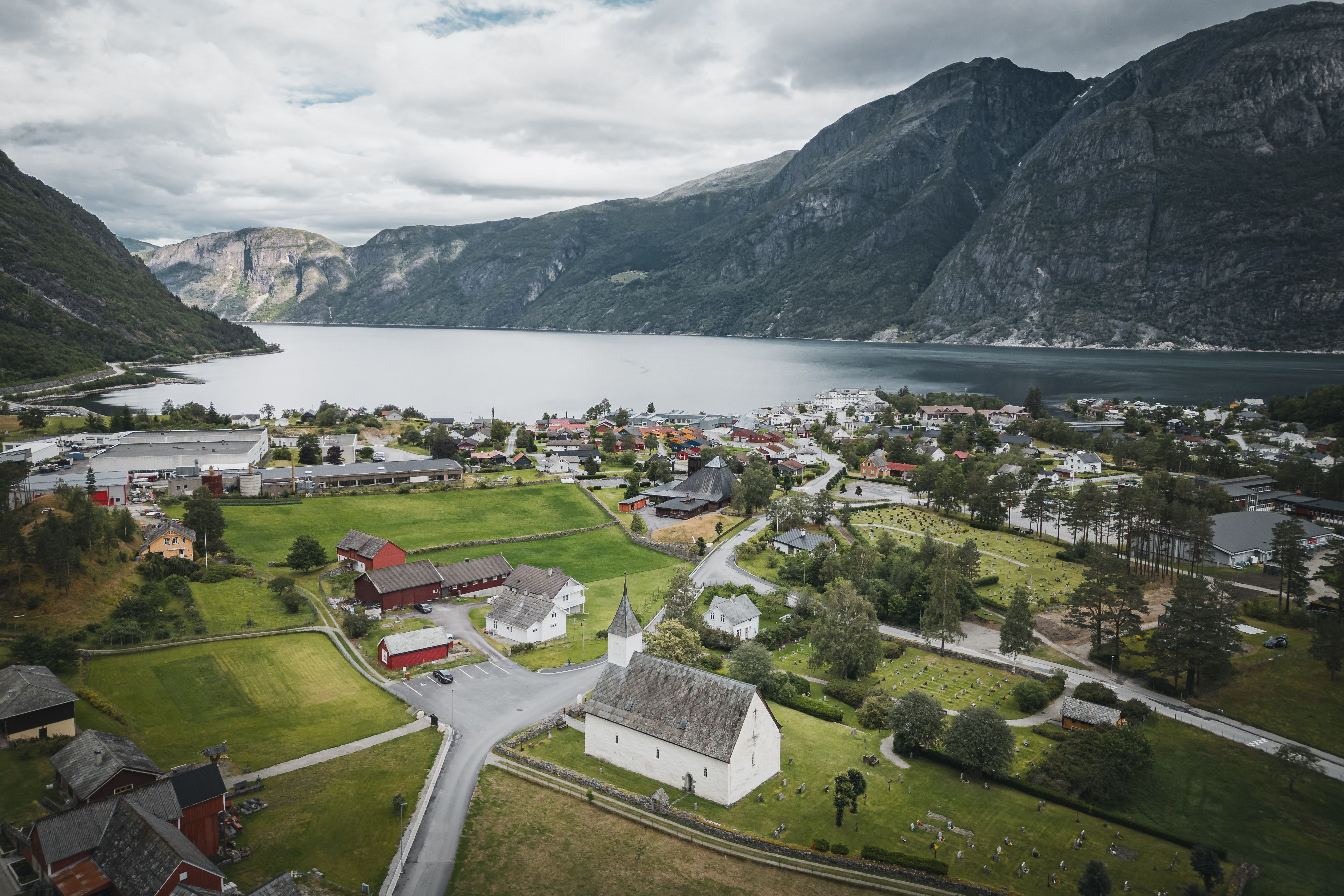 Ein Drohnenfoto der alten Kirche mit dem Fjord und den Bergen im Hintergrund.