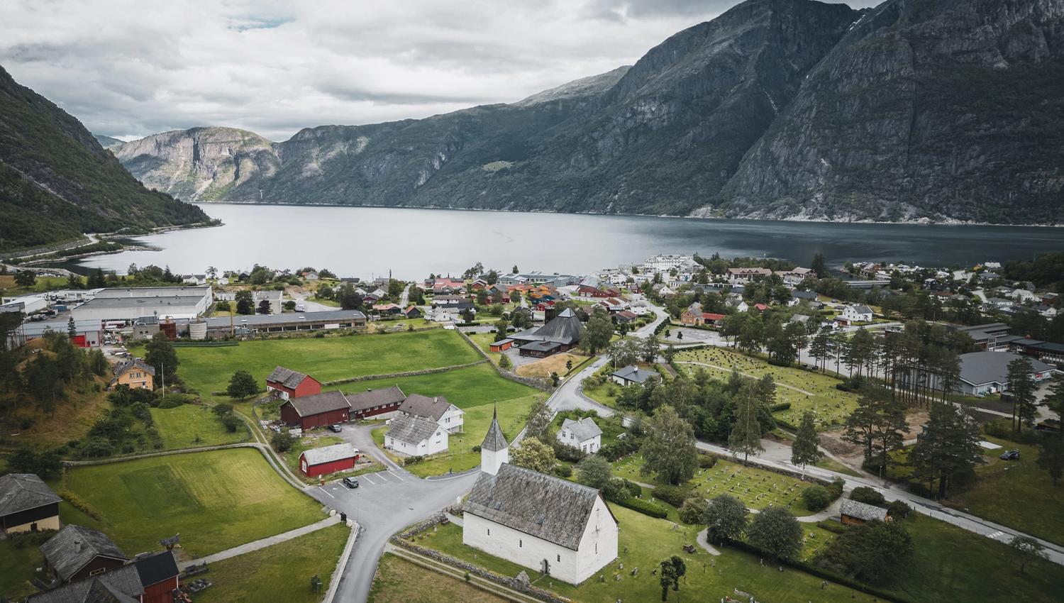 Ein Drohnenfoto der alten Kirche mit dem Fjord und den Bergen im Hintergrund.