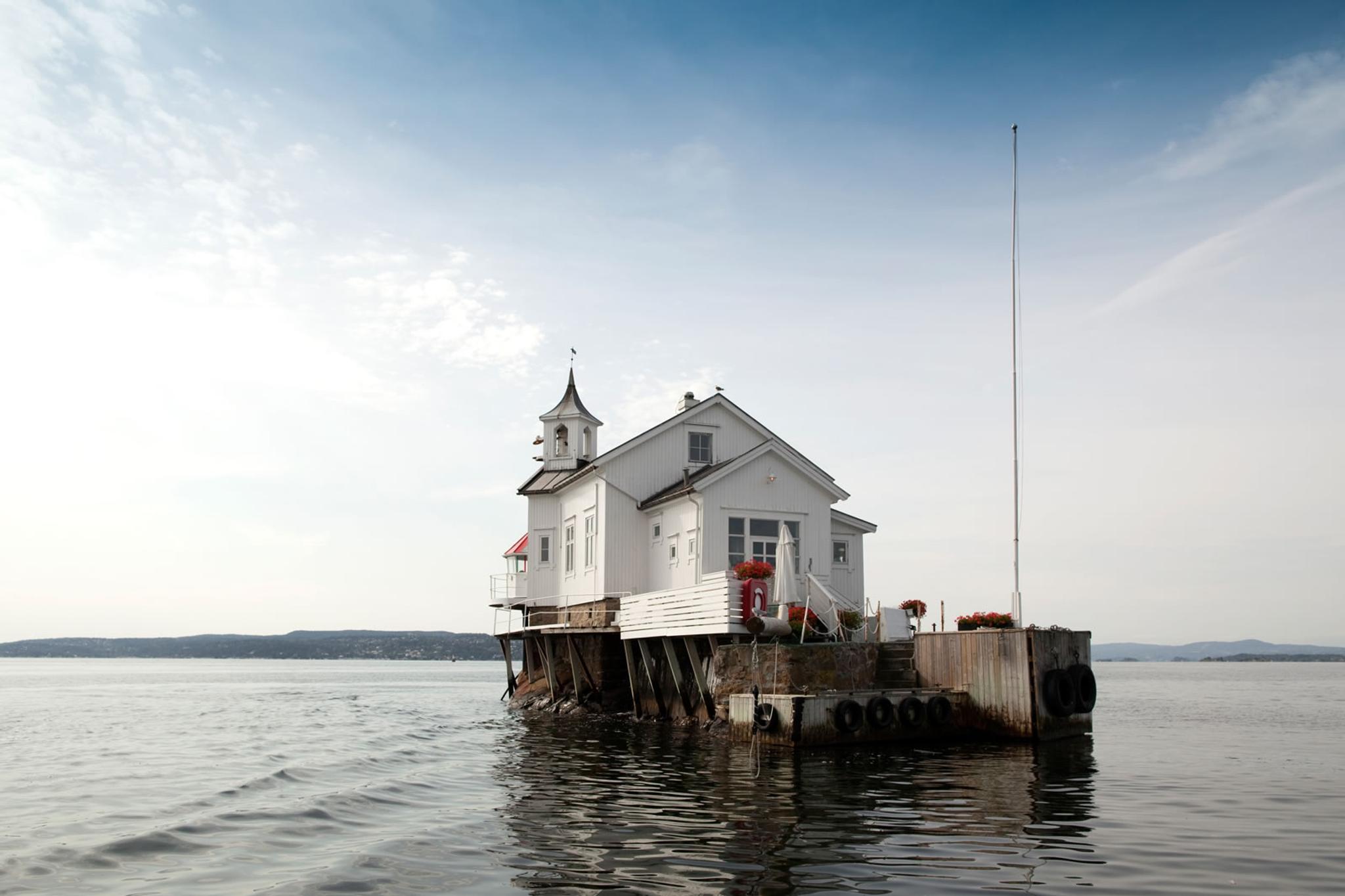 Dyna fyr exterior. Small, white wooden lighthouse, with flagpole and outdoor seating.