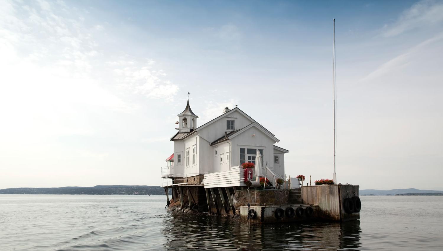 Dyna fyr exterior. Small, white wooden lighthouse, with flagpole and outdoor seating.