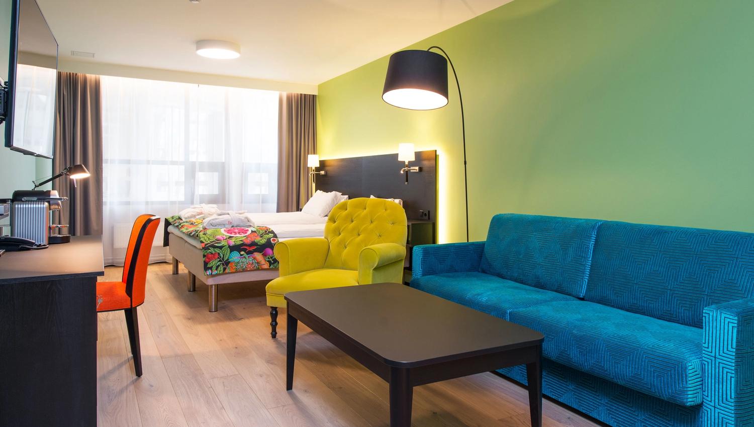 colourful double room with sofa, desk and TV
