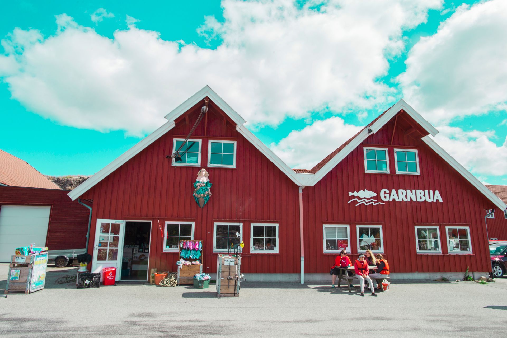 Fassade des Geschäfts Garnbua, ein großes rotes Gebäude mit weißen Leisten und Tür. Große weiße Buchstaben an der Wand schreiben „GARNBUA“, daneben ein Fisch.