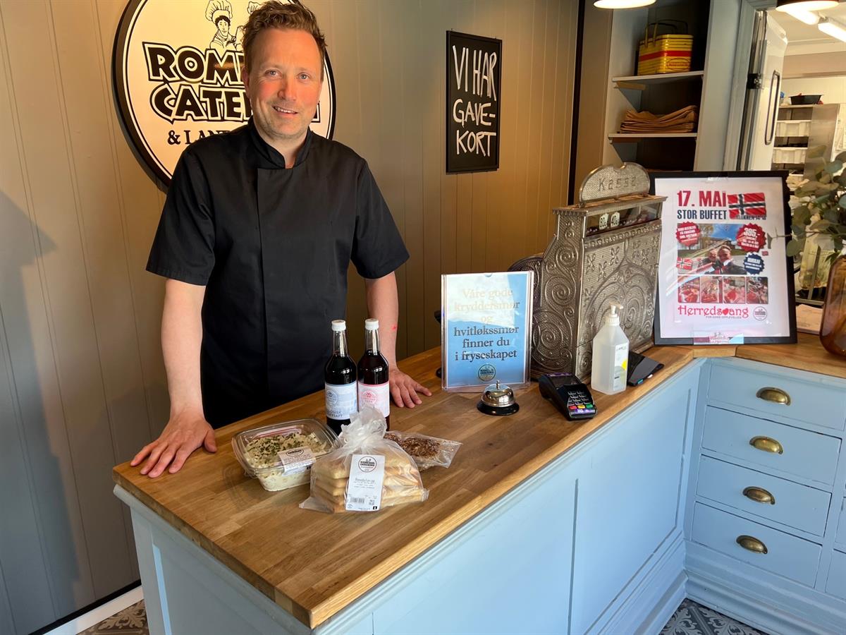 An employee standing behind a counter displaying local food products and a promotional sign.