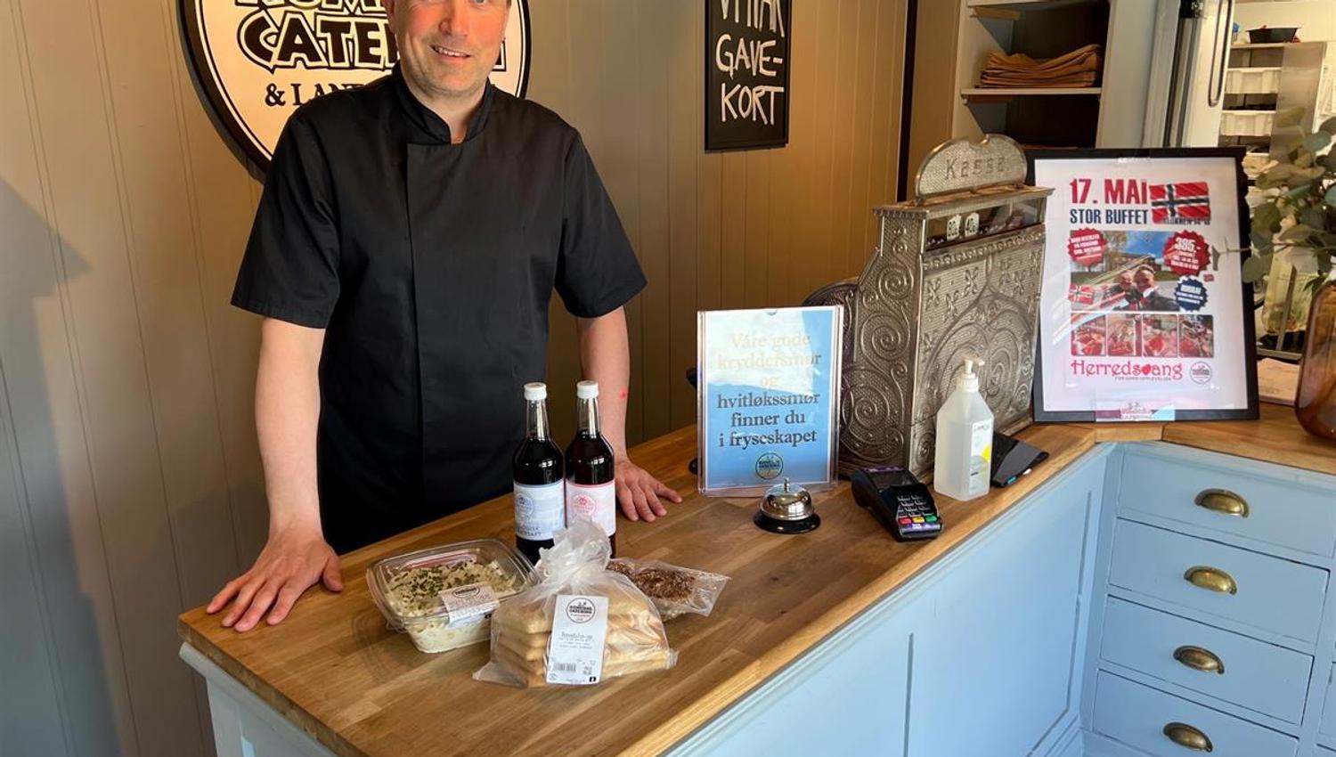 An employee standing behind a counter displaying local food products and a promotional sign.