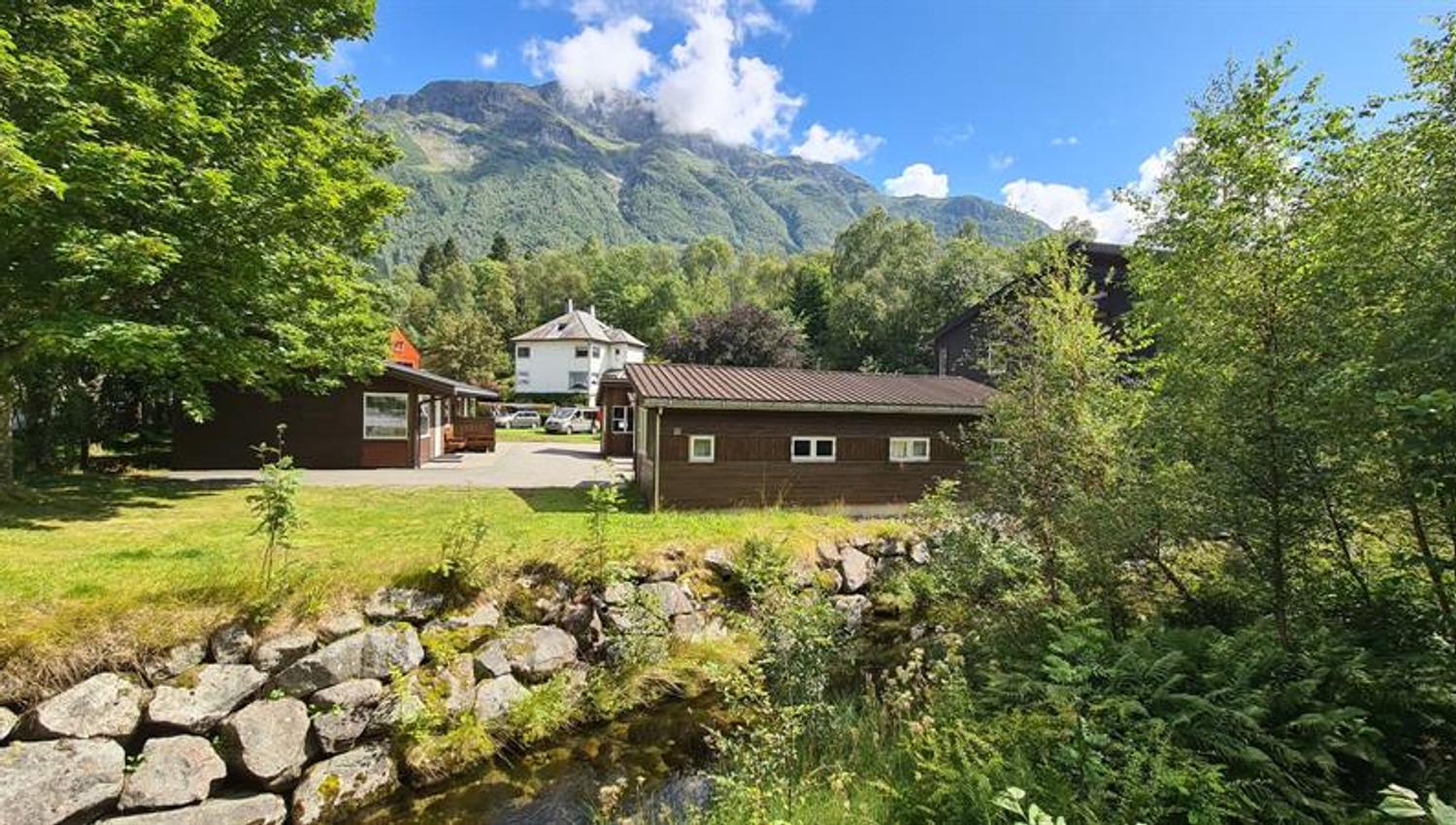 Cabins and service buildings at Trolltunga Camping with a small stream and lush surroundings.