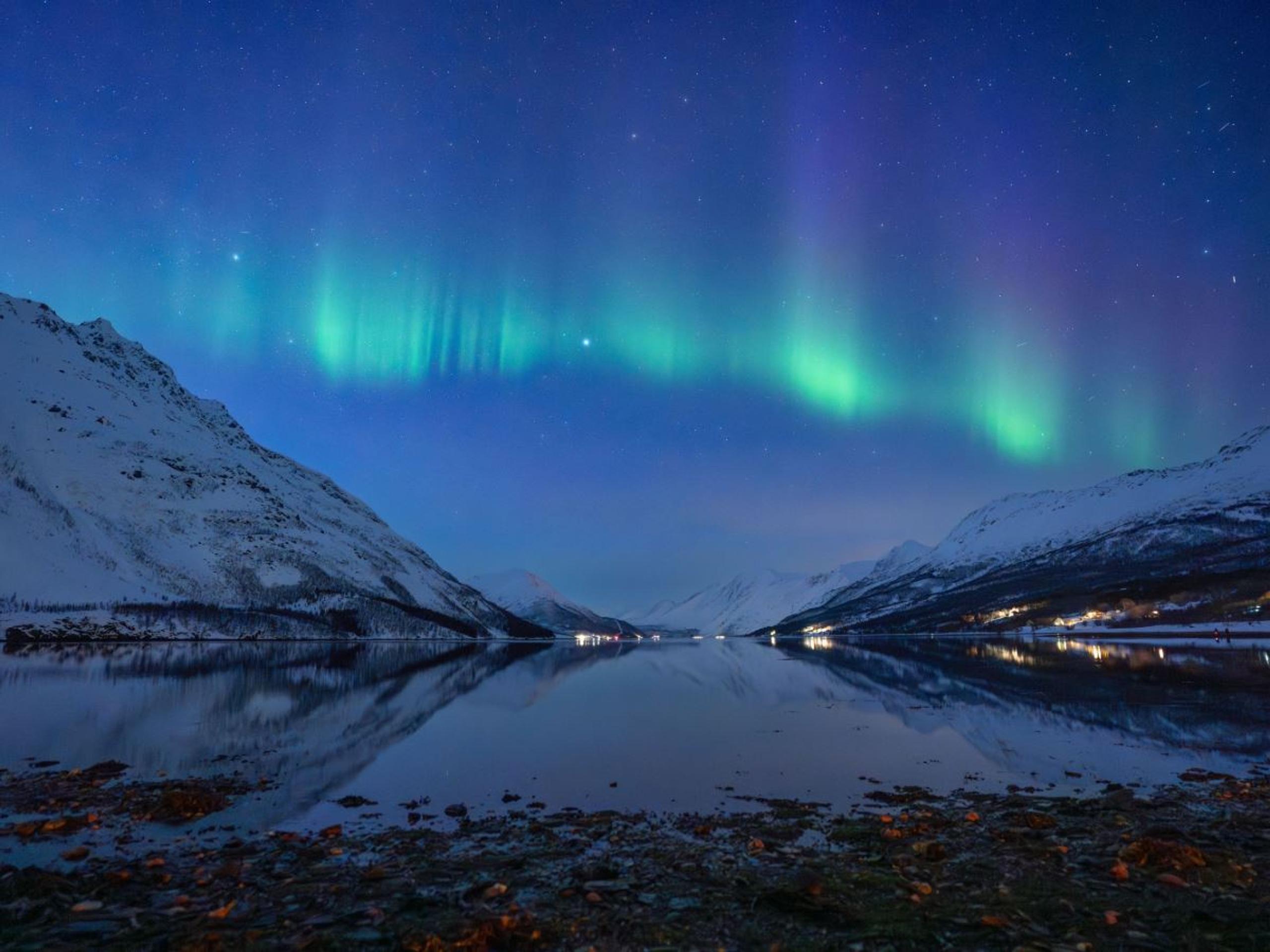 Green Northern Lights illuminate the night sky above an Arctic fjord and snow-covered mountains in Northern Norway. A natural phenomenon guests may be lucky enough to witness during their Northern Lights chas