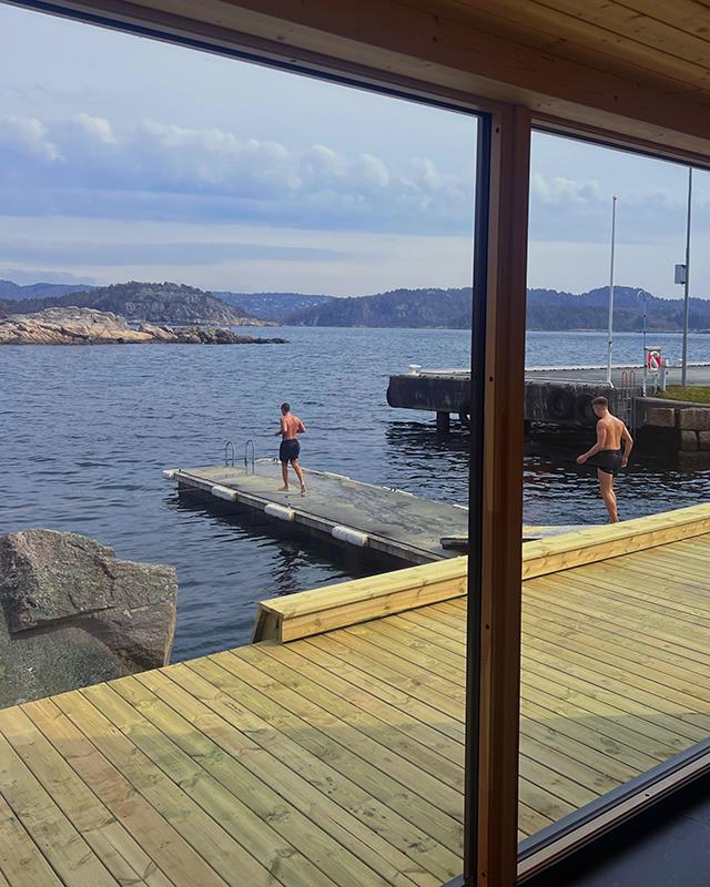 View through the sauna window, looking out at the sea and two people walking on the pier on their way to swim.
