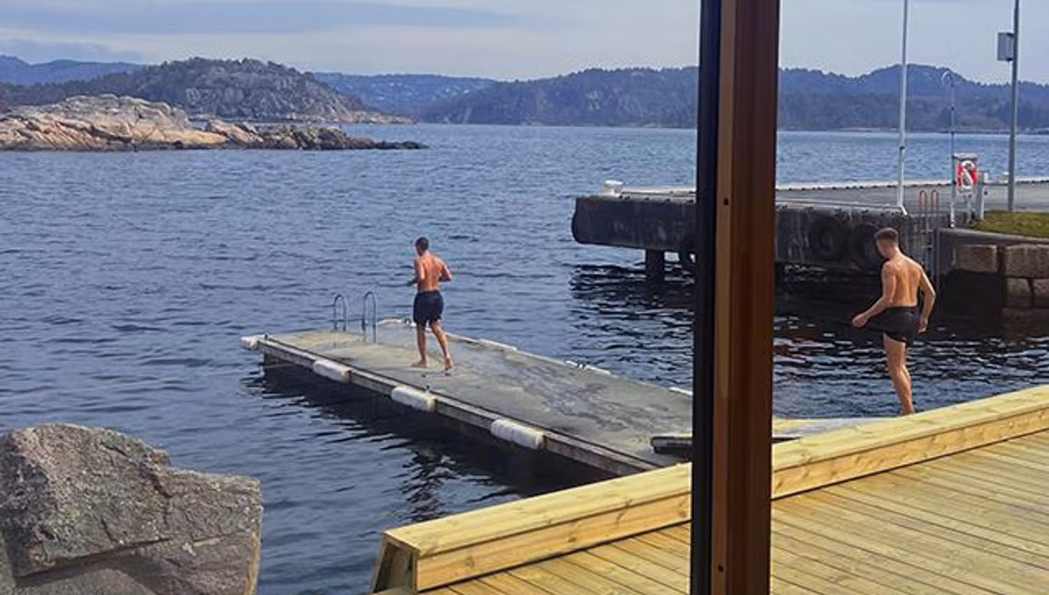 View through the sauna window, looking out at the sea and two people walking on the pier on their way to swim.