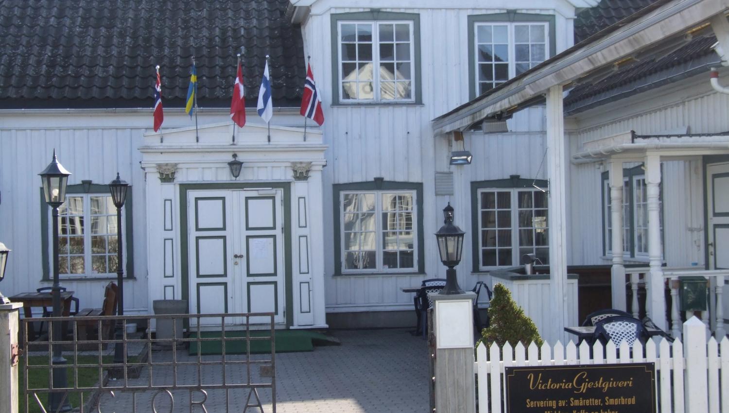 gammel hvit trebygning med blå vinduskarmer, smijernsport og flagg