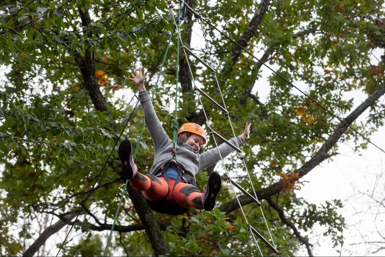 A happy girl strikes out with her arms hanging from the ladder under the trees