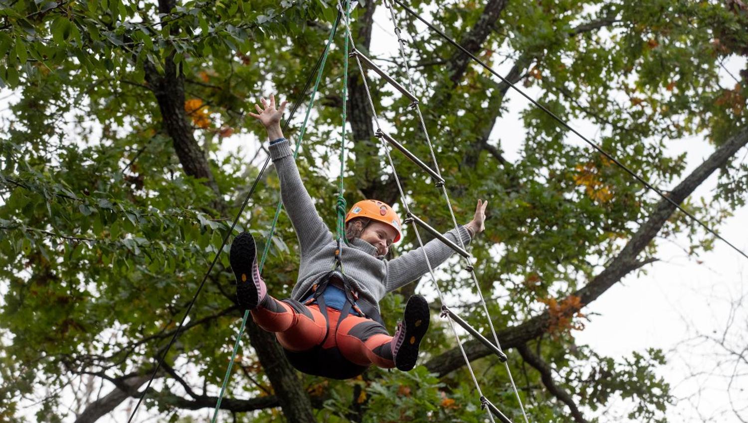 A happy girl strikes out with her arms hanging from the ladder under the trees