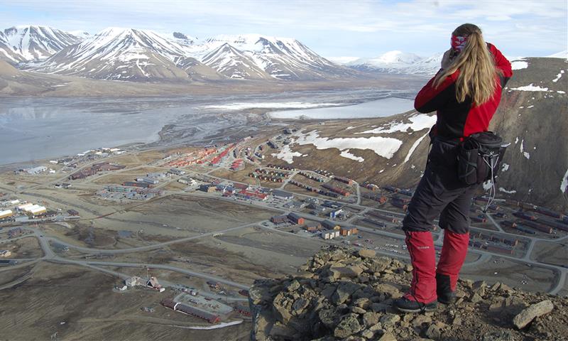 A person standing on top of Platåfjellet looking down on the buildings in Longyearbyen in the background